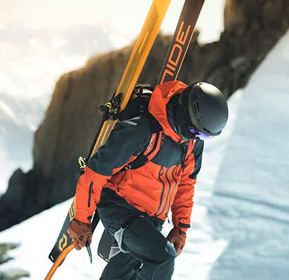 model sa ski oprekom ruksakom i skijama na ruksaku sa kacigom i brilama ski pogledom prema dolje i bijeloj pozadini